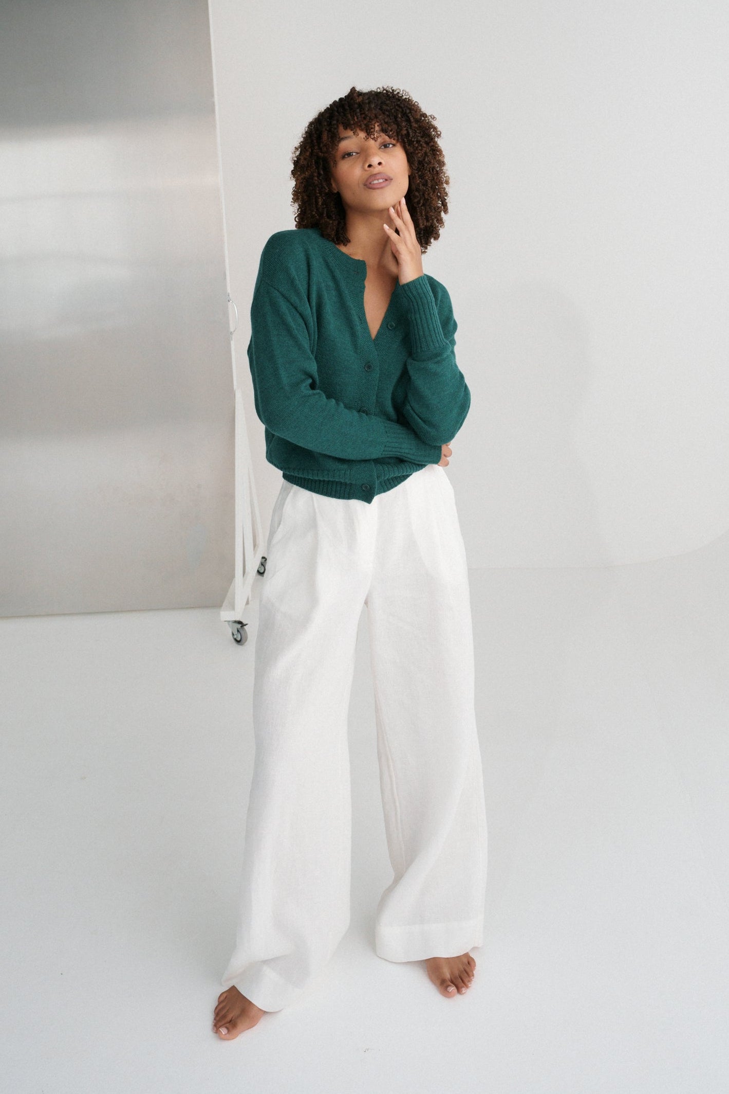 LILLY PILLY woman wearing pine green coloured Taylor merino knit cardigan and white pants in a minimalistic setting