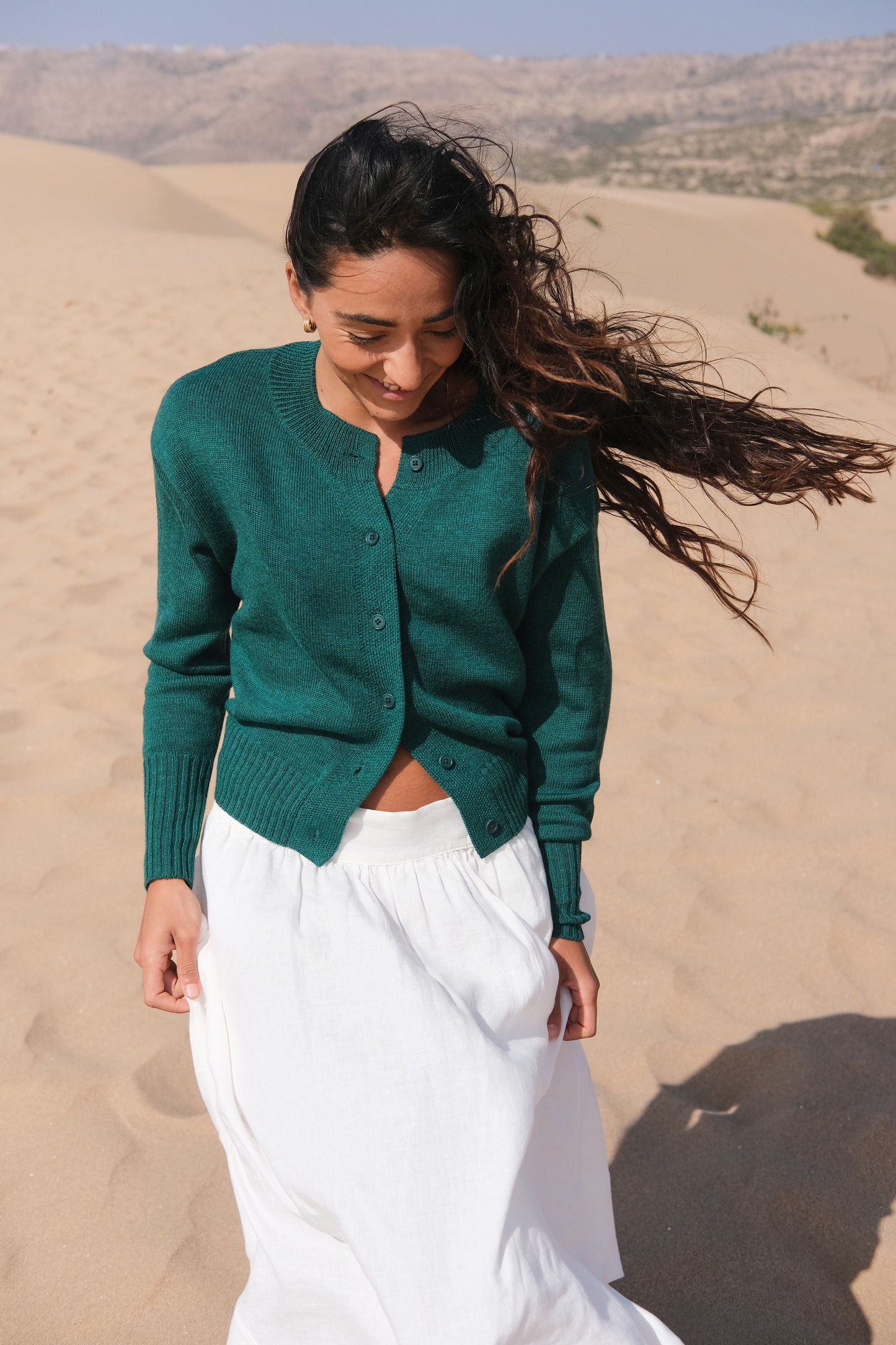 LILLY PILLY woman wearing pine green coloured Taylor merino knit cardigan standing in sand dunes with mountains in the background