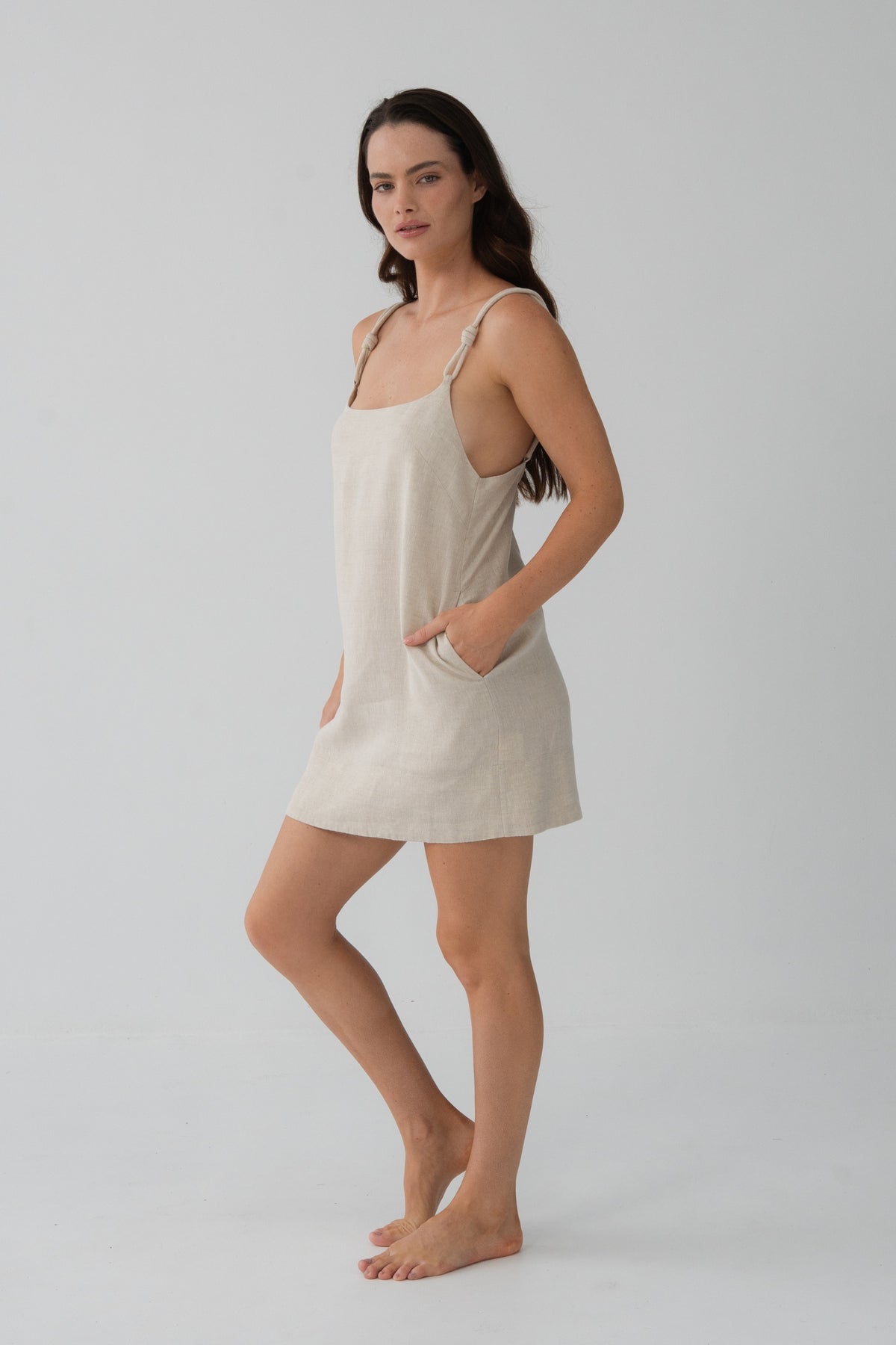 Tevi Linen Short Slip Dress in Oatmeal - three-quarter view, hands in pockets, side pockets detail - Lilly Pilly Collection