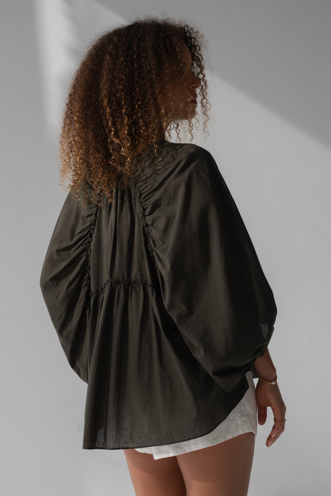 Woman wearing a dark green blouse with balloon sleeves on a plain background