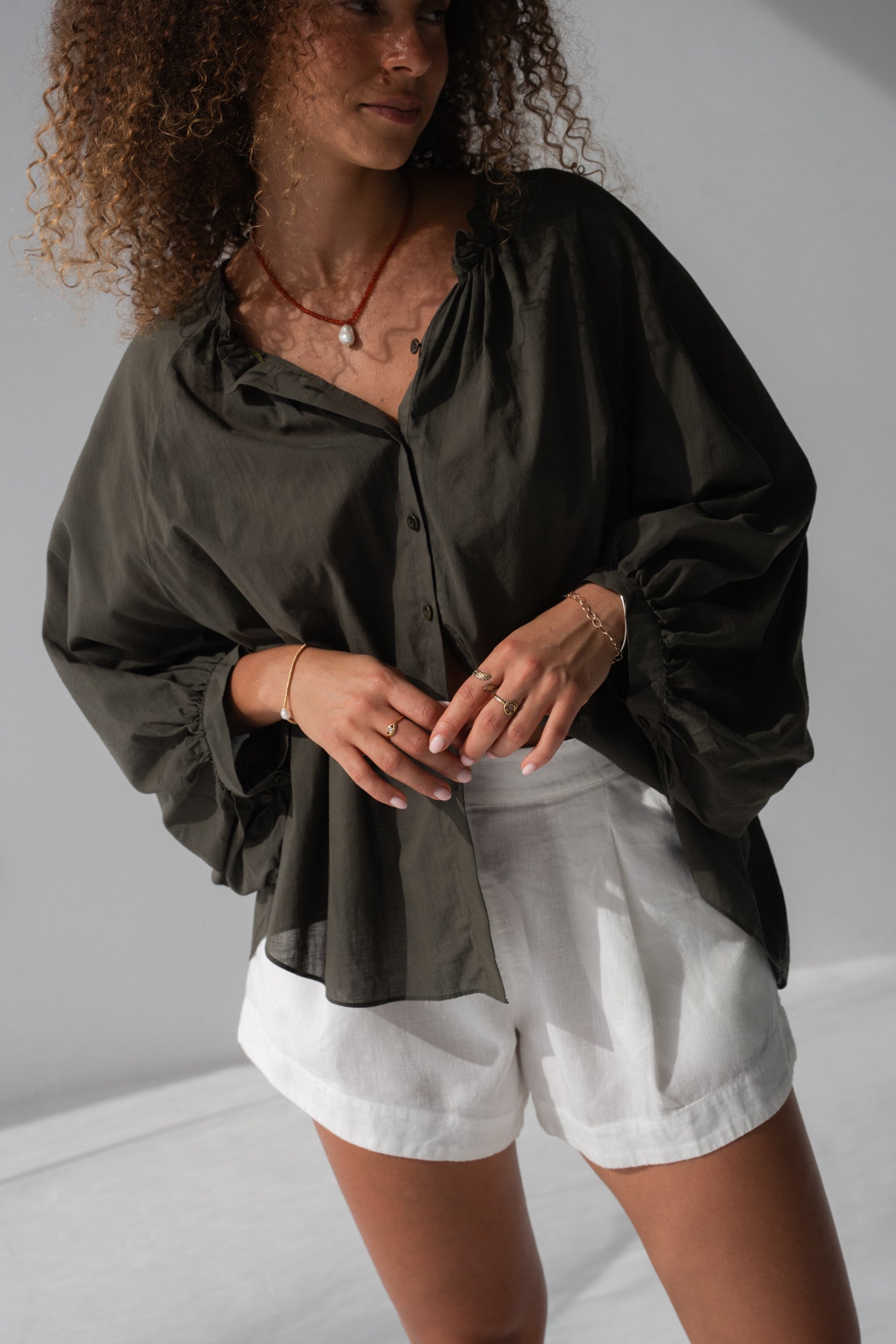Woman wearing a dark green blouse and white shorts against a plain background