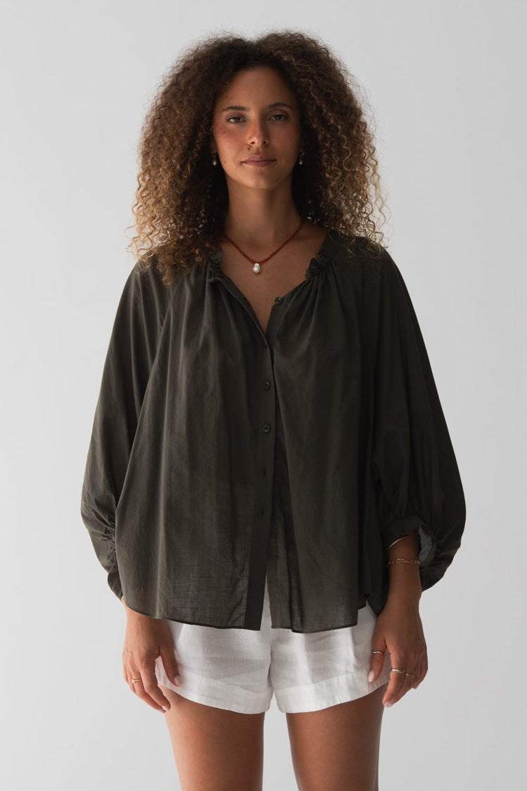 Woman wearing a dark green blouse and white shorts against a plain background