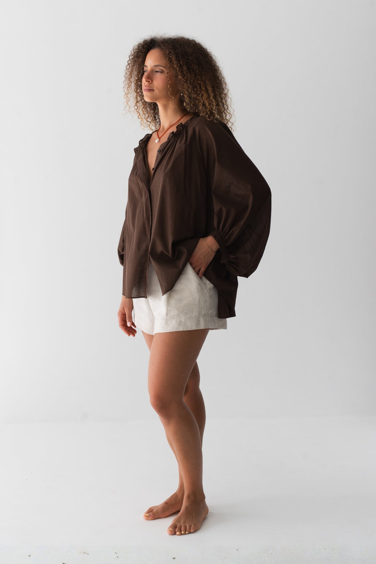 Thalia Cotton Voile Shirt in Chocolate - side view, gathered neckline and balloon sleeves, worn over Gaia Linen Shorts in Oatmeal - Lilly Pilly Collection
