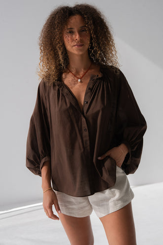 Thalia Cotton Voile Shirt in Chocolate - front view, gathered neckline and button-front, balloon sleeves, hand in pocket, worn over Gaia Linen Shorts in Oatmeal - Lilly Pilly Collection