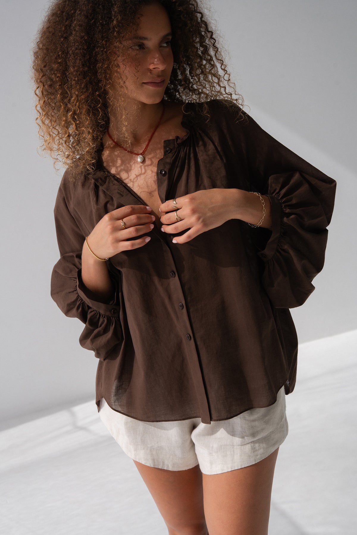 Thalia Cotton Voile Shirt in Chocolate - close-up, gathered neckline and button-front detail, balloon sleeves, worn over Gaia Linen Shorts in Oatmeal - Lilly Pilly Collection