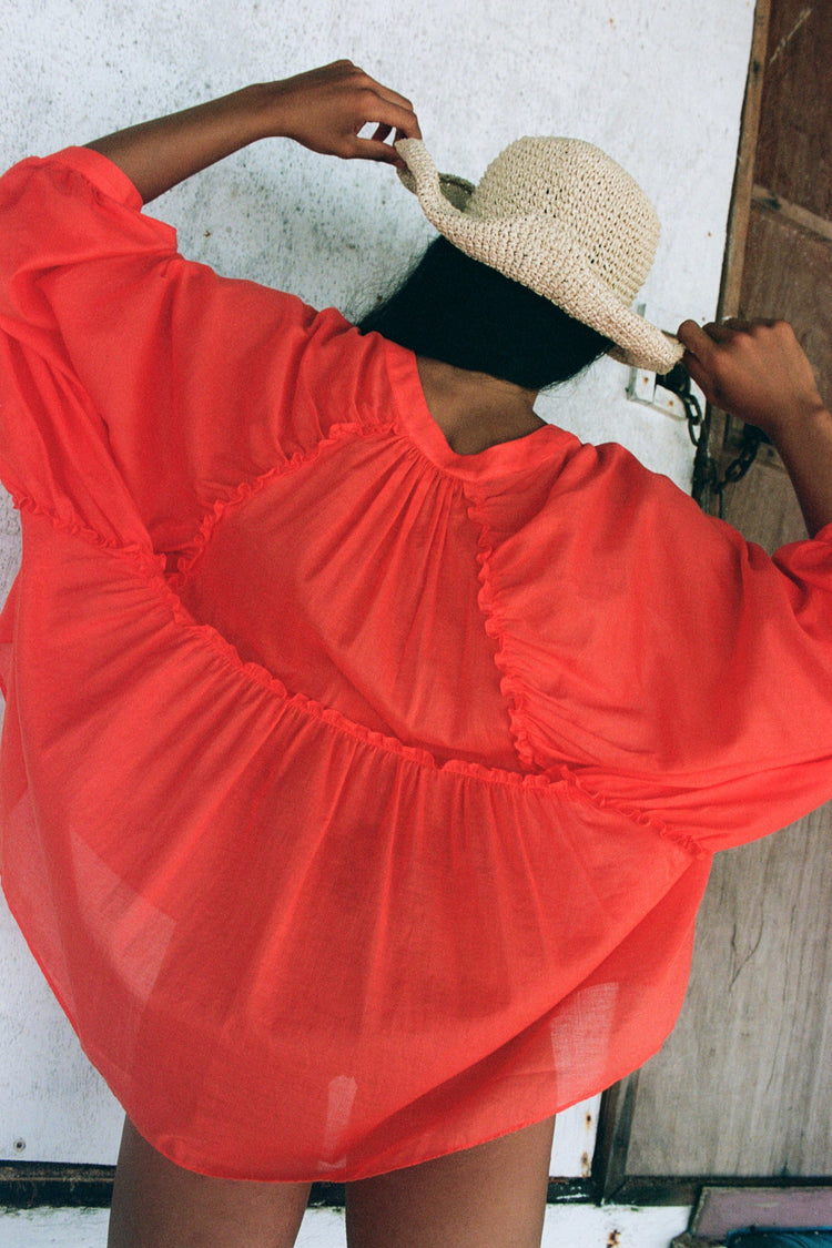 Thalia Cotton Voile Shirt in Spritz Orange - back view, gathered back yoke and balloon sleeves, worn open as beach cover-up, straw hat, rustic white wall backdrop - Lilly Pilly Collection