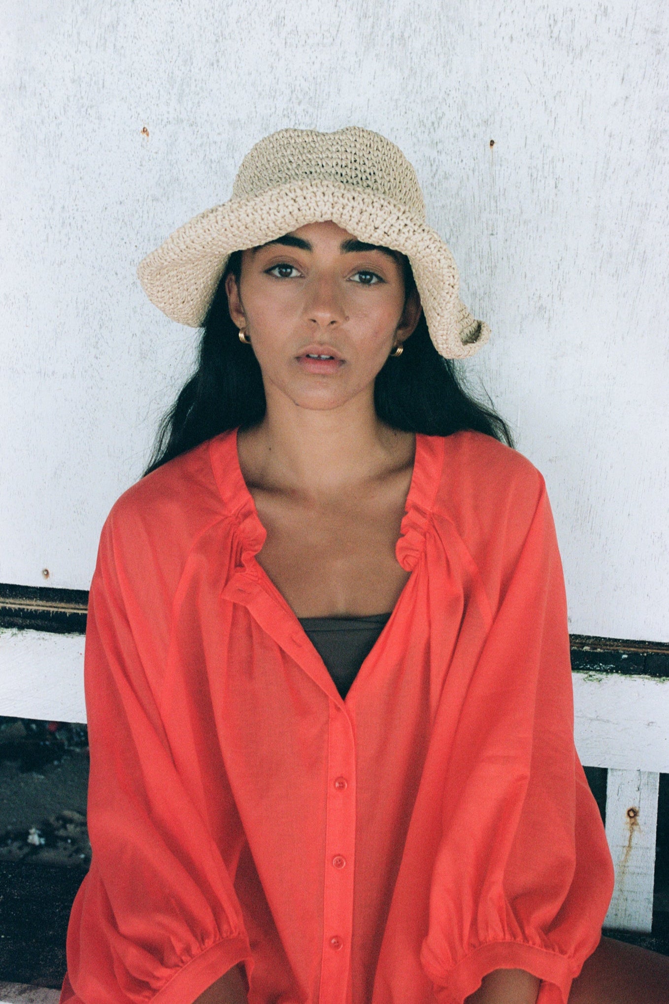 Close up of LILLY PILLY woman wearing a spritz Thalia cotton voile shirt wearing a straw hat against a white wall.