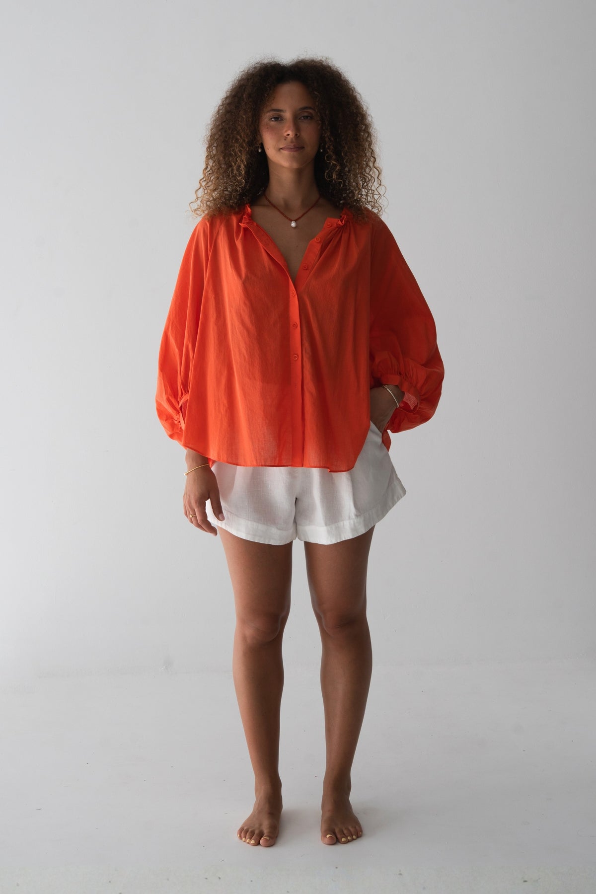 Thalia Cotton Voile Shirt in Spritz Orange - front view, gathered neckline and button-front, balloon sleeves, worn open over white linen shorts - Lilly Pilly Collection