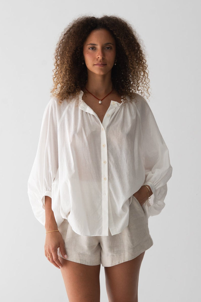 LILLY PILLY woman wearing a ivory Thalia cotton voile shirt blouse and oatmeal-coloured Gaia shorts against a plain background