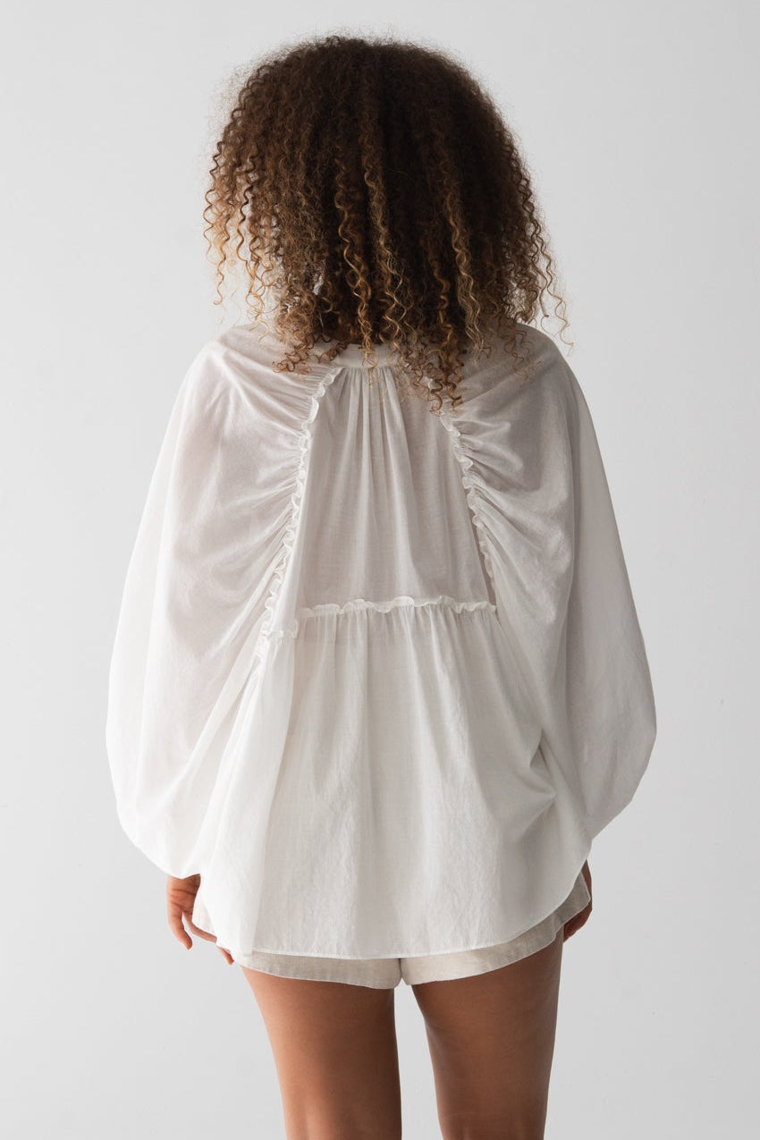 Close up back view of LILLY PILLY woman wearing a ivory Thalia cotton voile shirt blouse and oatmeal-coloured Gaia shorts against a neutral background