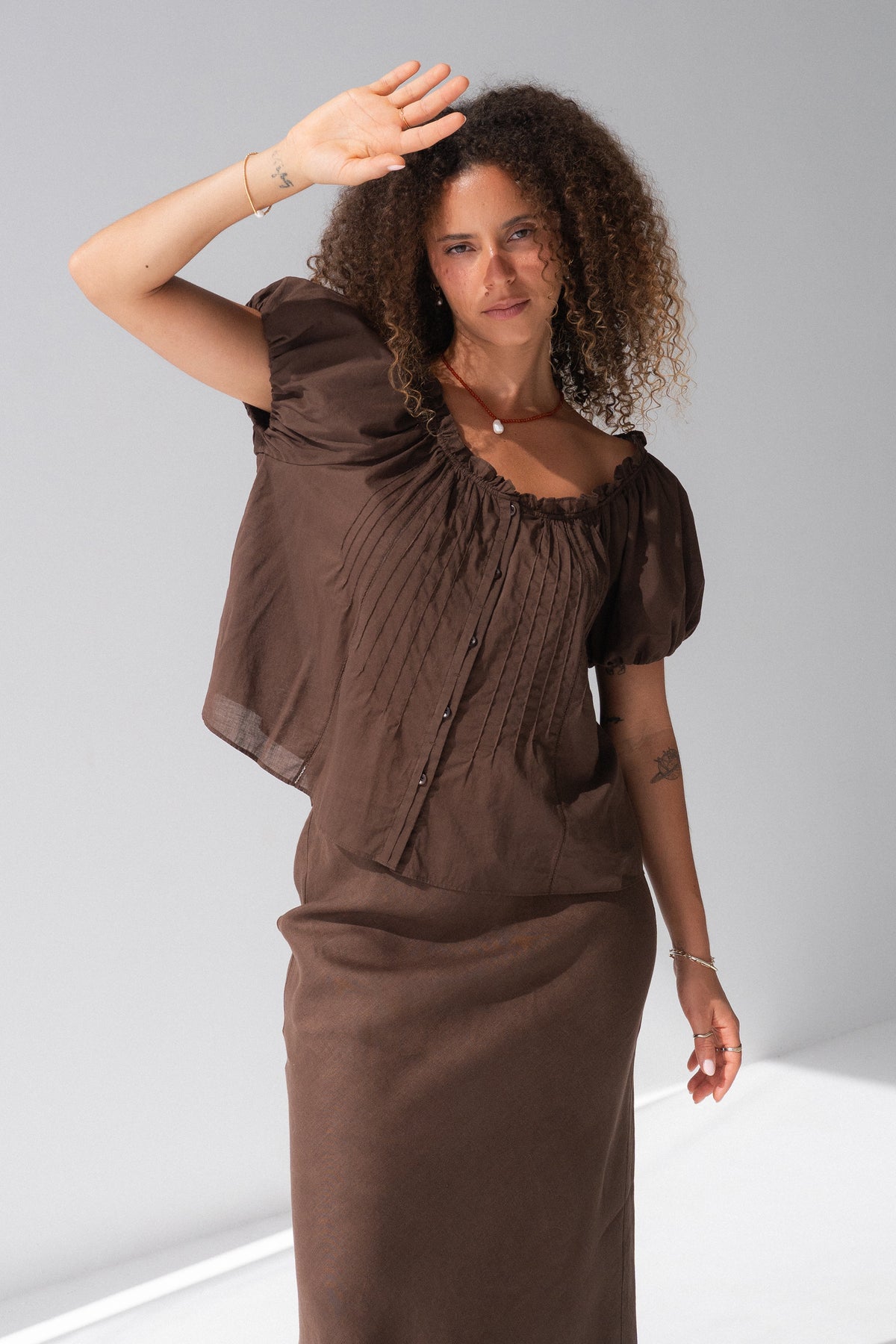 Tilly Cotton Voile Shirt in Chocolate - full length, gathered ruffle neckline and pintuck detail, puff sleeves, worn with matching Riley Bias Linen Midi Skirt in Chocolate, arm raised - Lilly Pilly Collection