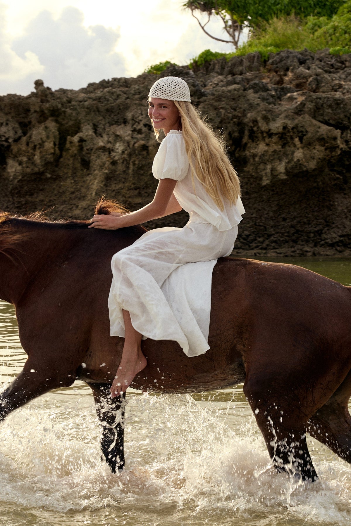 Tilly Cotton Voile Shirt in Ivory - woman riding horse through ocean, worn with Stella Linen Maxi Skirt in Ivory, crochet bucket hat, rocky coastline backdrop - Lilly Pilly Collection