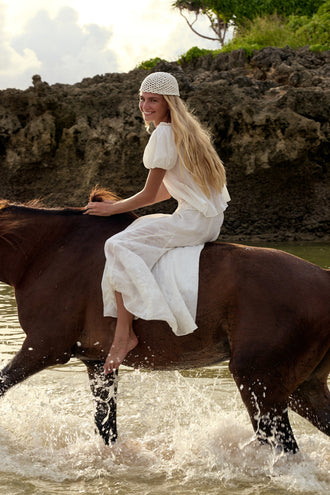 Tilly Cotton Voile Shirt in Ivory - woman riding horse through ocean, worn with Stella Linen Maxi Skirt in Ivory, crochet bucket hat, rocky coastline backdrop - Lilly Pilly Collection