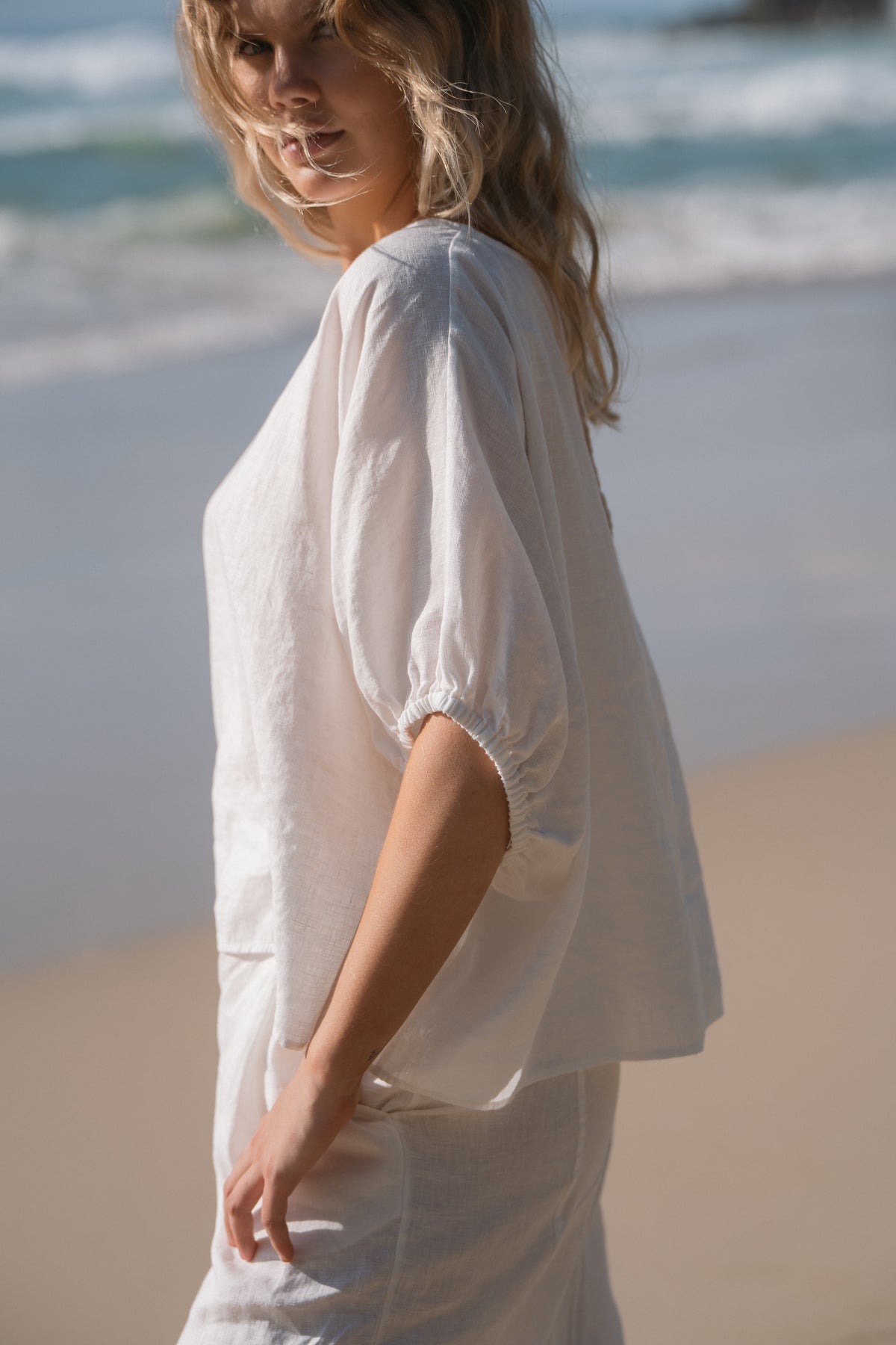 Tina Linen Top in Ivory - side profile close-up of the sleeve, beach backdrop - Lilly Pilly Collection