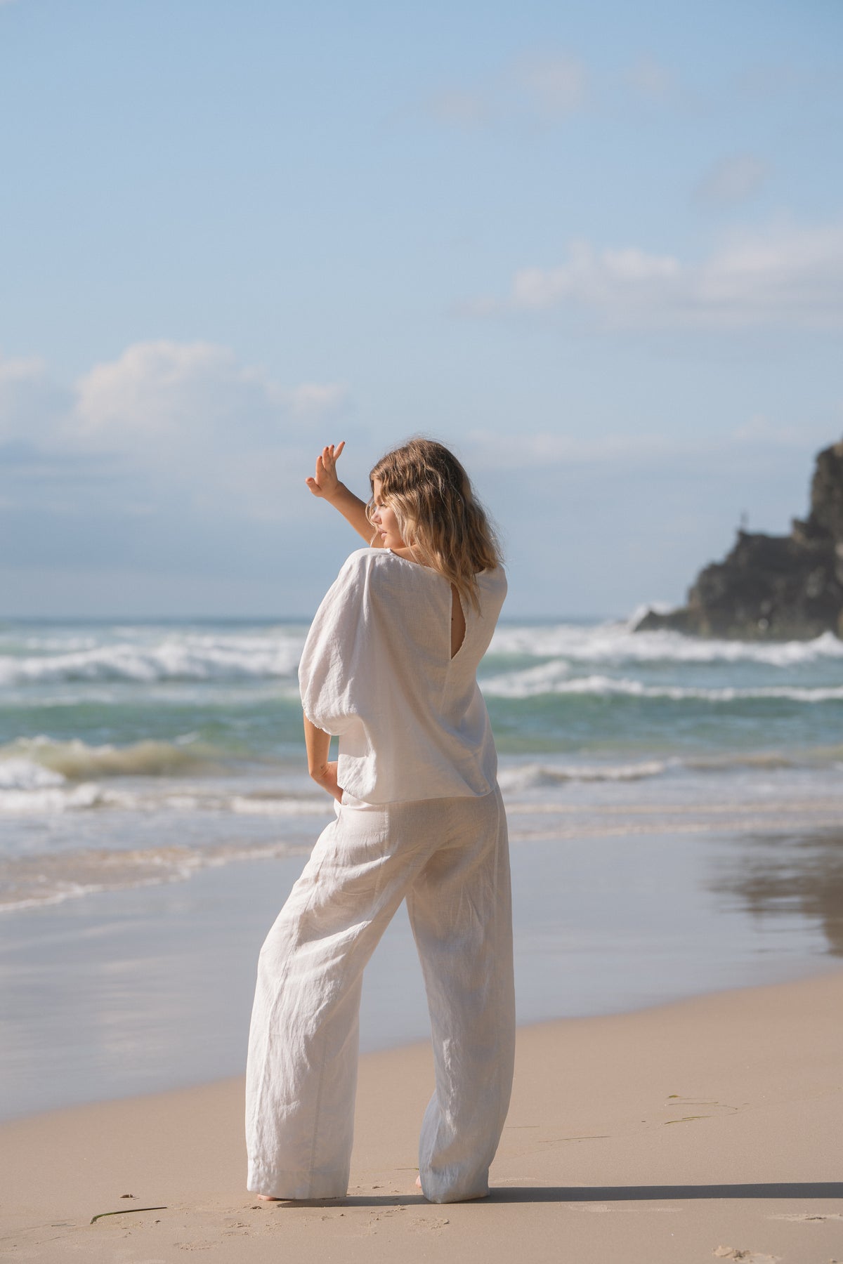 Tina Linen Top in Ivory - back view, keyhole cutout, styled with wide-leg pants, standing at the shoreline - Lilly Pilly Collection