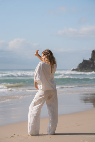 Tina Linen Top in Ivory - back view, keyhole cutout, styled with wide-leg pants, standing at the shoreline - Lilly Pilly Collection