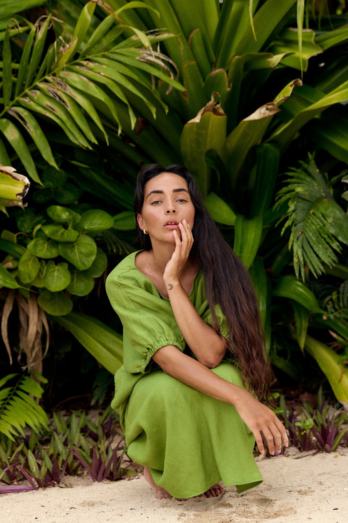 Tina Linen Top in Lime Green - woman crouching on beach, close-up of puff sleeve and round neckline, tropical greenery backdrop - Lilly Pilly Collection