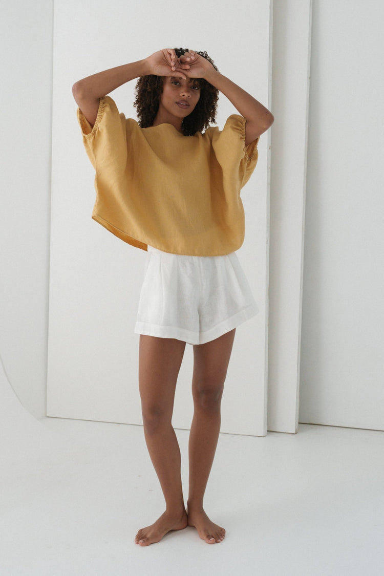 Tina Linen Top in Sand - full length front view, arms raised, batwing silhouette, styled with white linen shorts - Lilly Pilly Collection