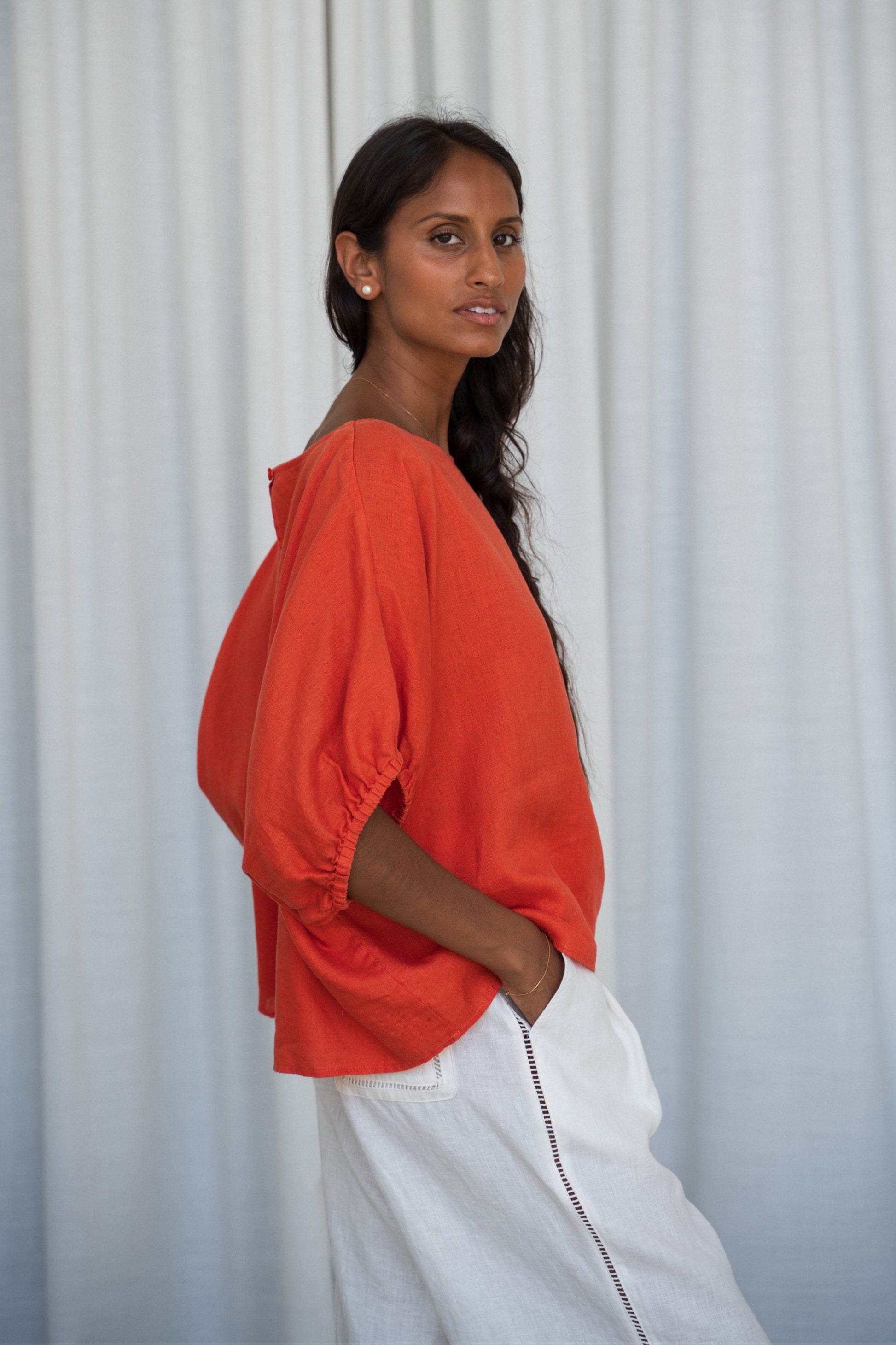 Person wearing a Leia linen top in Spritz and ivory Oli linen pants against a white curtain background side view