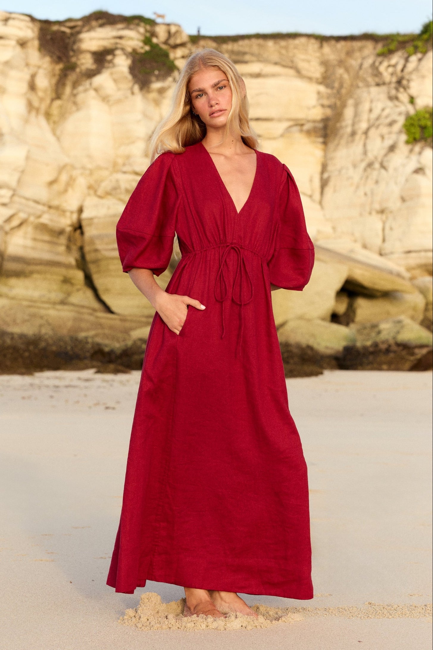 Front view of a woman wearing the Vida Linen maxi dress in Cherry Red on the sand - Lilly Pilly Collection