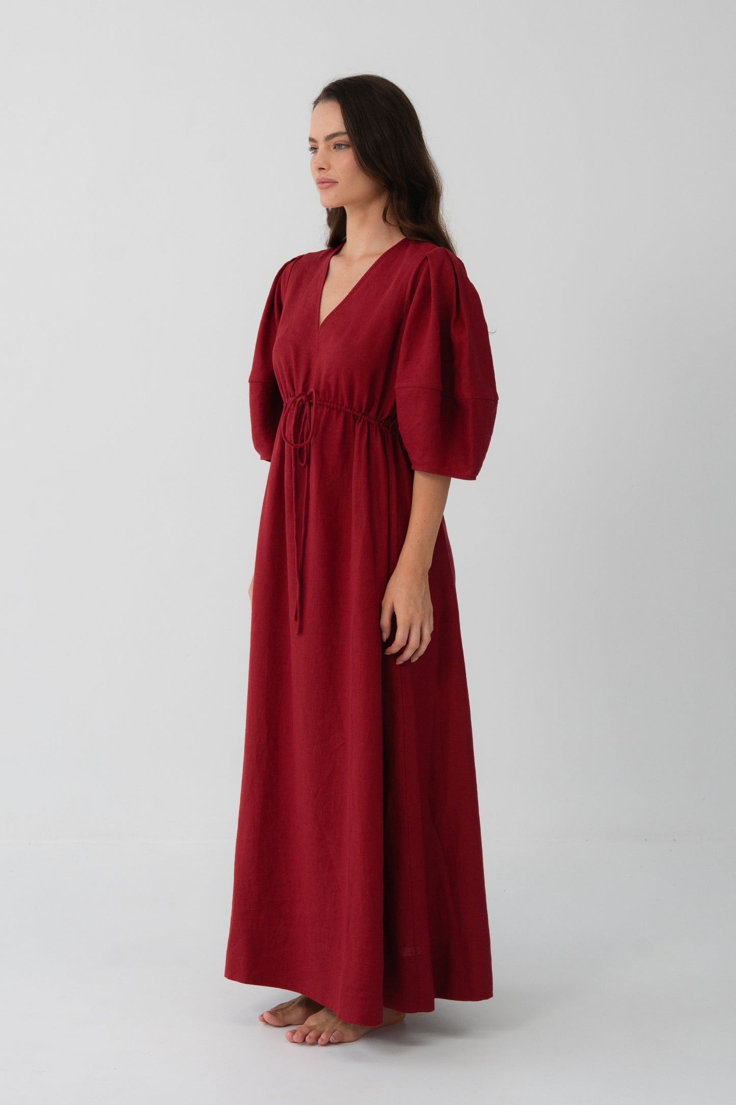 Side angle view of a woman wearing the Vida Linen maxi dress in Cherry Red in a studio setting - Lilly Pilly Collection