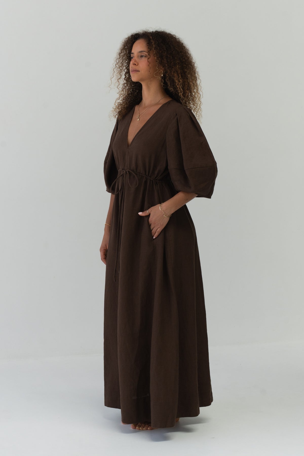 Side view of a woman wearing the Vida Linen maxi dress in Chocolate in a studio - Lilly Pilly Collection