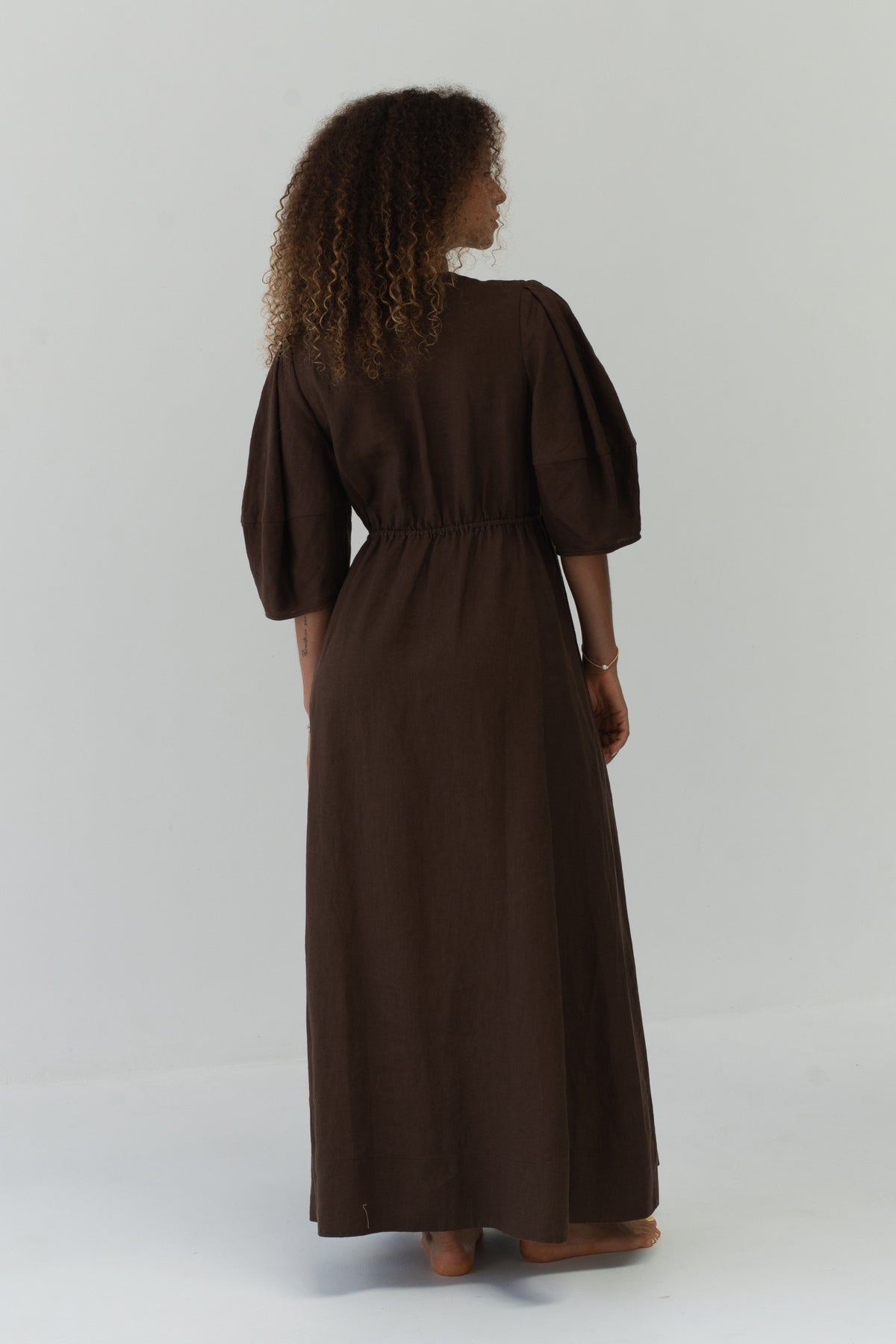 Back view of a woman wearing the Vida Linen maxi dress in Chocolate in a studio - Lilly Pilly Collection