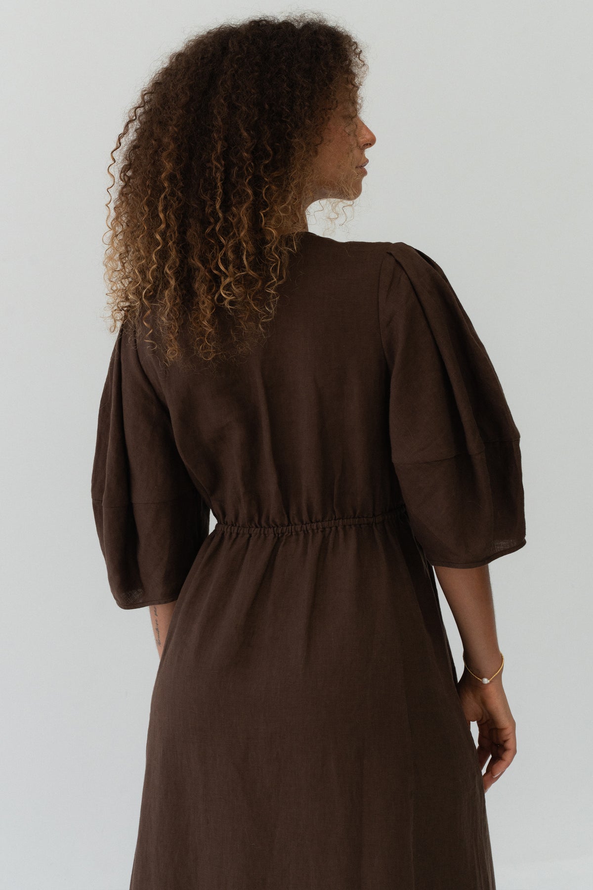 Back view of a woman wearing the Vida Linen maxi dress in Chocolate in a studio setting - Lilly Pilly Collection