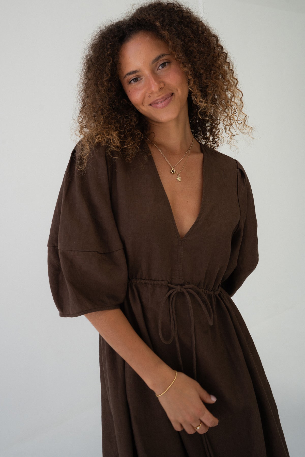 Close-up front view of a smiling woman wearing the Vida Linen maxi dress in Chocolate in a studio setting - Lilly Pilly Collection