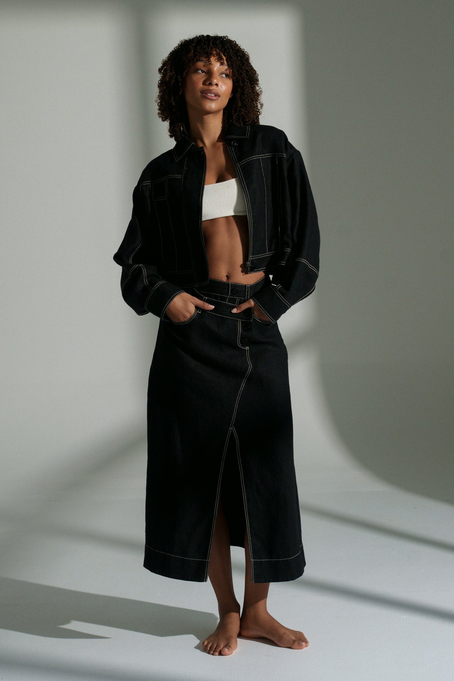LILLY PILLY woman wearing a black Wes linen jacket standing in a minimalistic setting with light casting shadows.