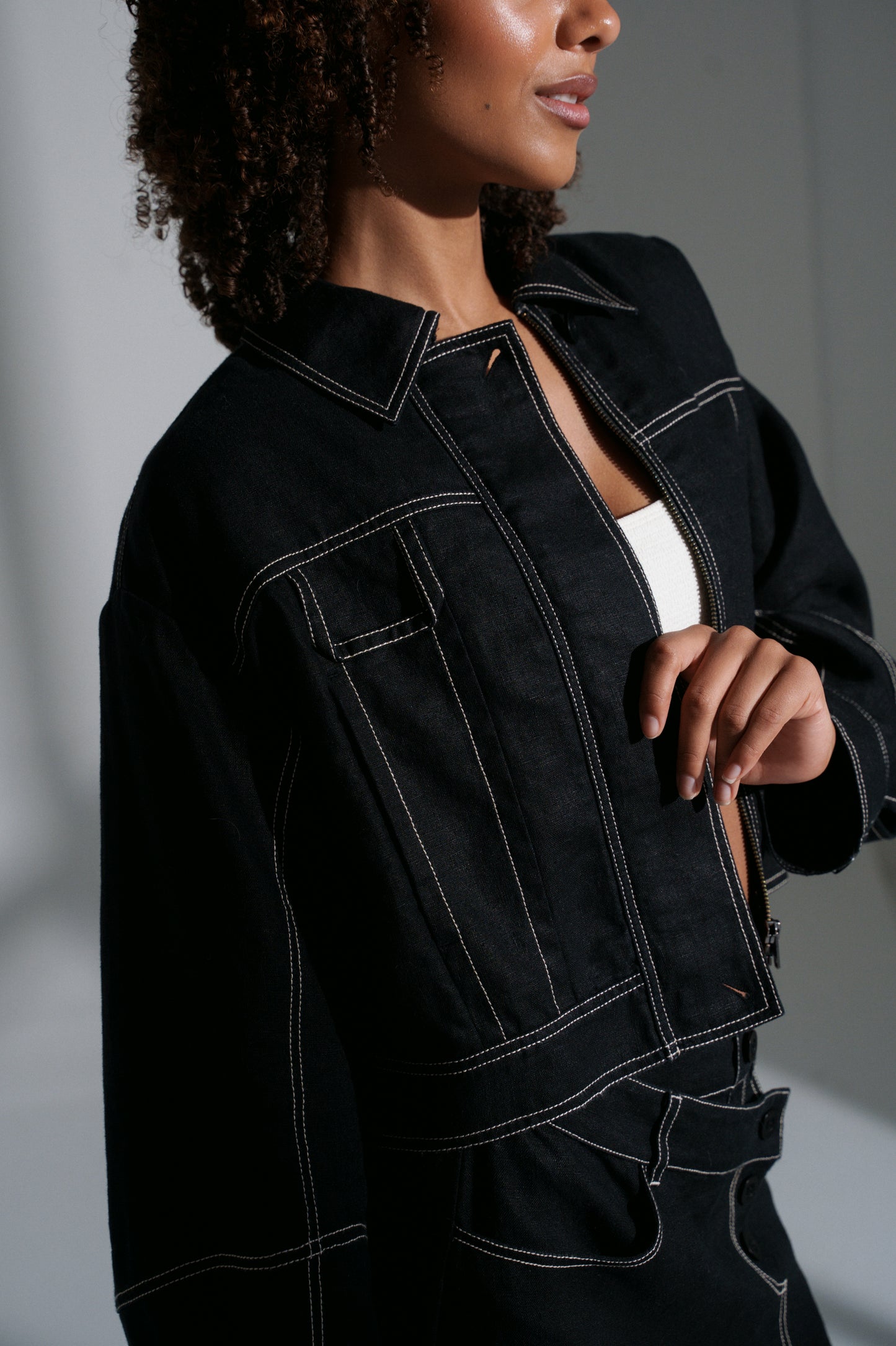 LILLY PILLY woman wearing a black Wes linen jacket with white stitching on a neutral background