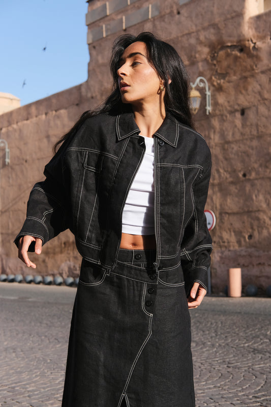 LILLY PILLY woman wearing a black Wes linen jacket standing by a textured wall.
