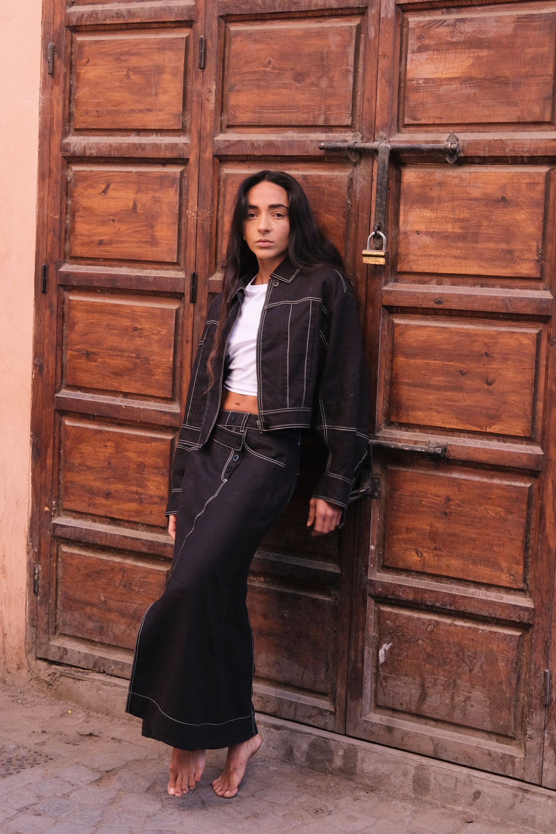LILLY PILLY woman wearing a black Wes linen jacket standing in front of a large wooden door