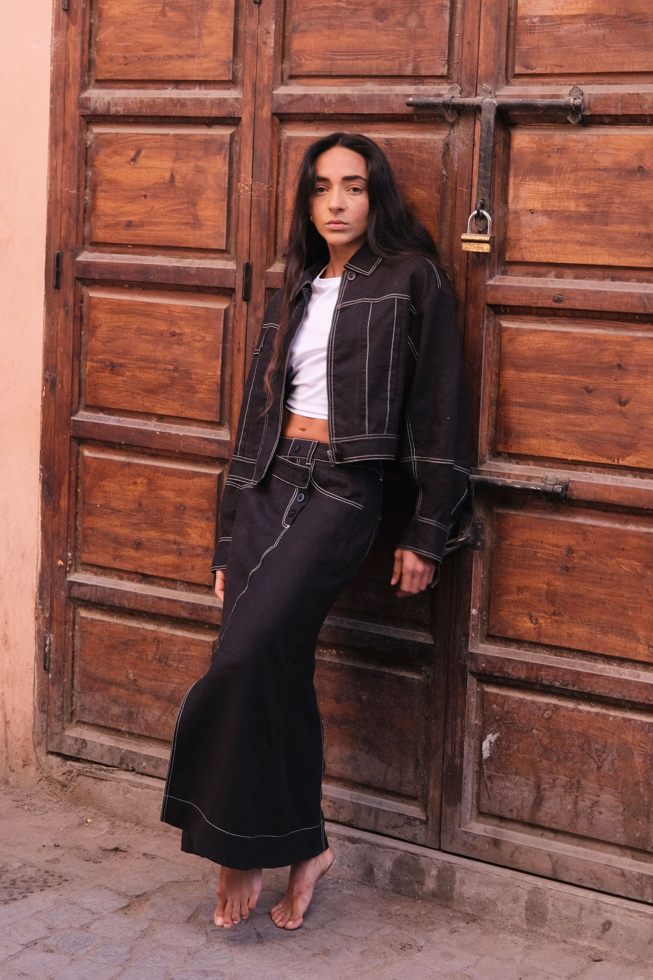 LILLY PILLY woman wearing a black Wes linen jacket and Jax linen skirt standing in front of a large wooden door