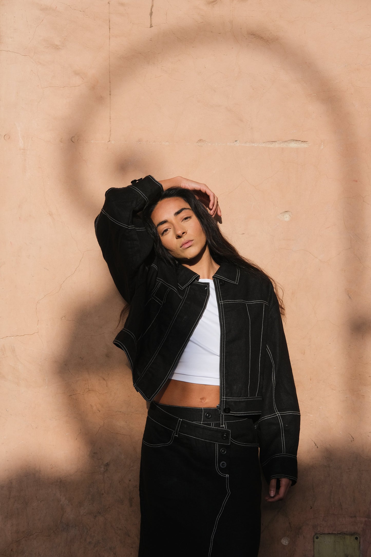 LILLY PILLY woman wearing a black Wes linen jacket and white top against a textured beige wall