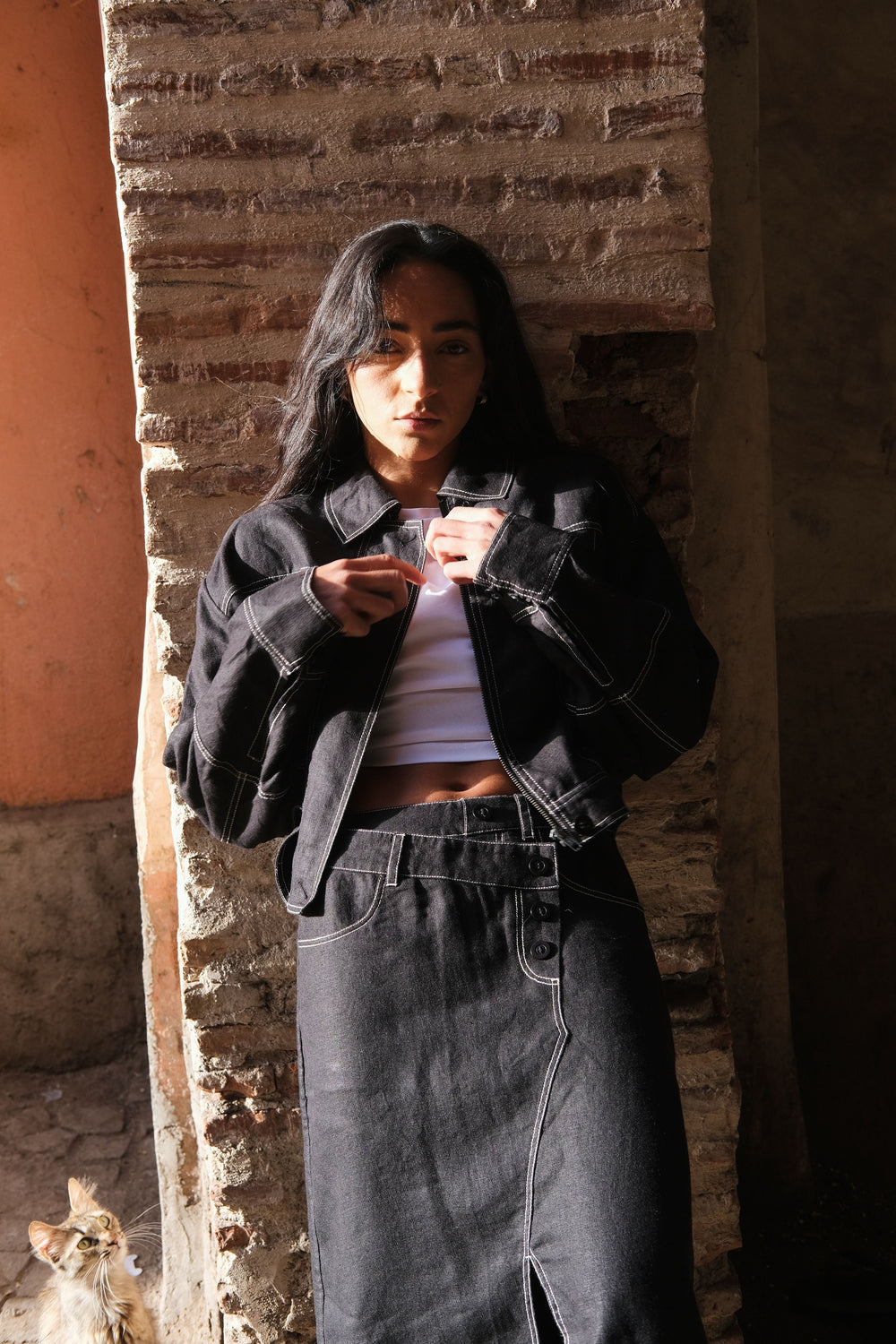 LILLY PILLY woman wearing a black Wes linen jacket standing against a textured wall.