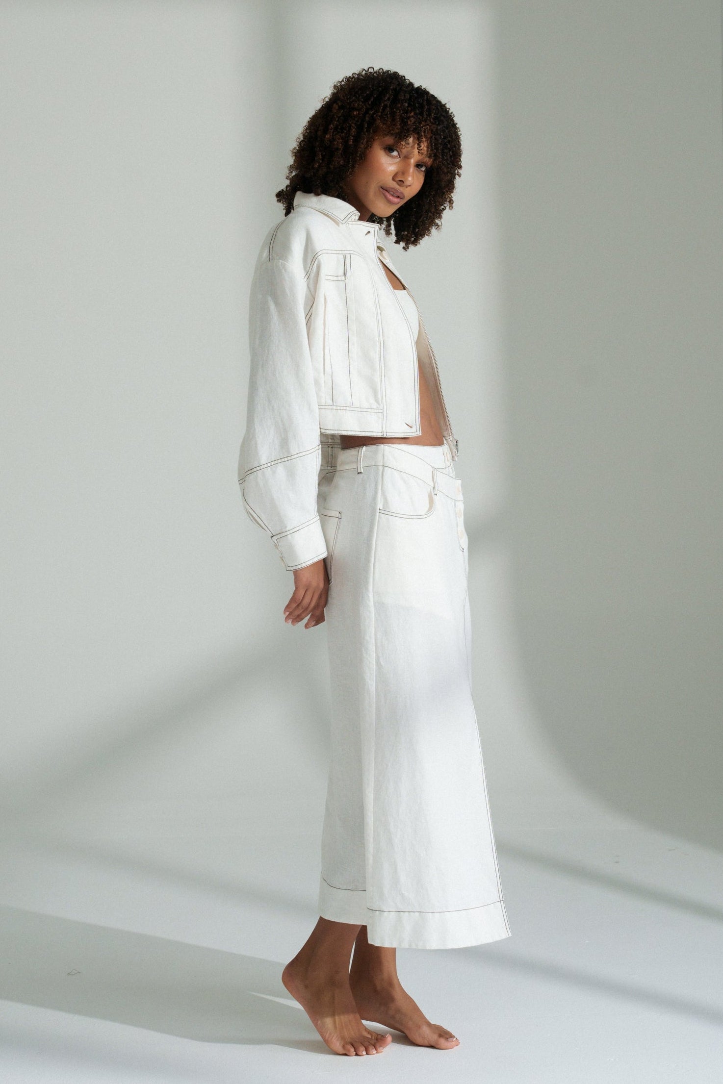 LILLY PILLY woman wearing an ivory Wes linen jacket standing against a plain white background