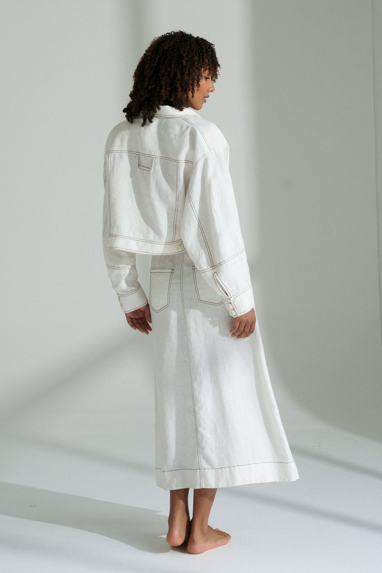 LILLY PILLY woman wearing an ivory Wes linen jacket standing in a minimalistic room with light gray walls.