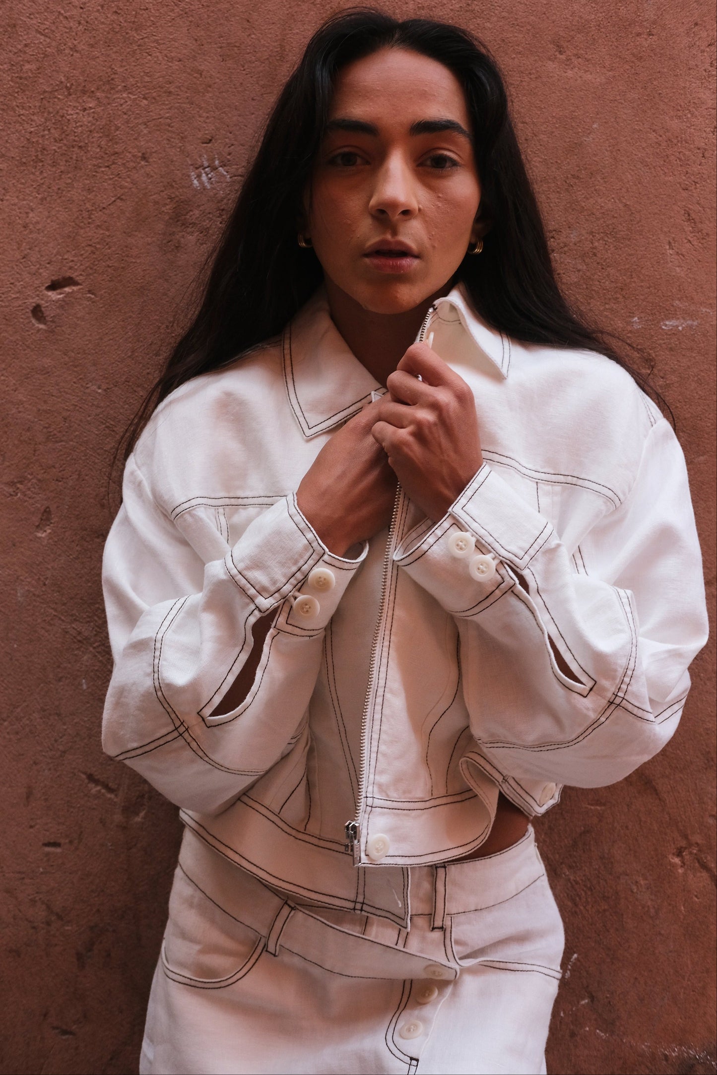 LILLY PILLY woman wearing an ivory Wes linen jacket against a brown wall