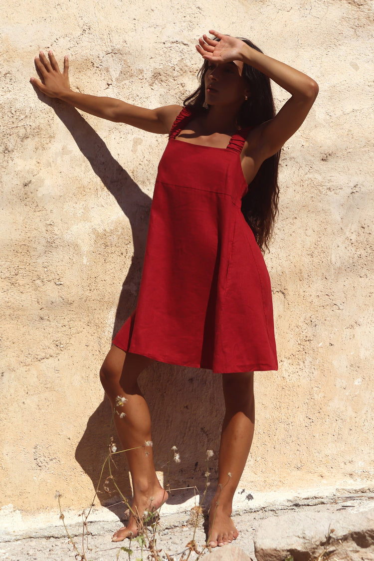 Zahra Linen Mini Dress in Cherry Red - woman against sandstone wall, arms raised, ruched straps and A-line skirt - Lilly Pilly Collection