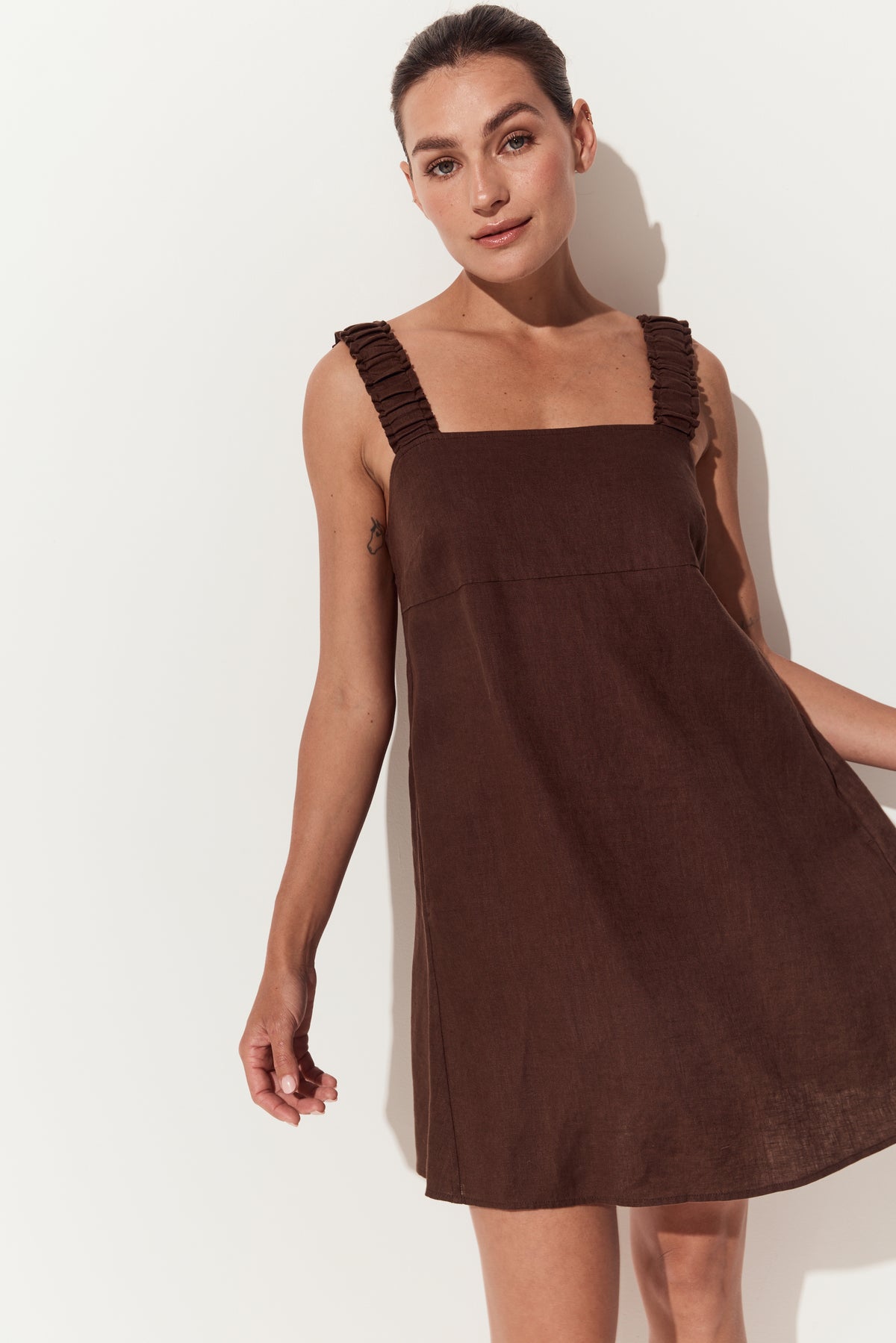 Zahra Linen Mini Dress in Chocolate - front view with hand fanning dress to the side - Lilly Pilly Collection