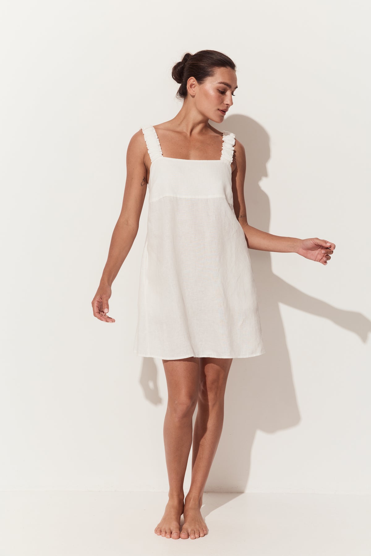 Zahra Linen Mini Dress in Ivory - three quarter view while standing by a white studio wall - Lilly Pilly Collection