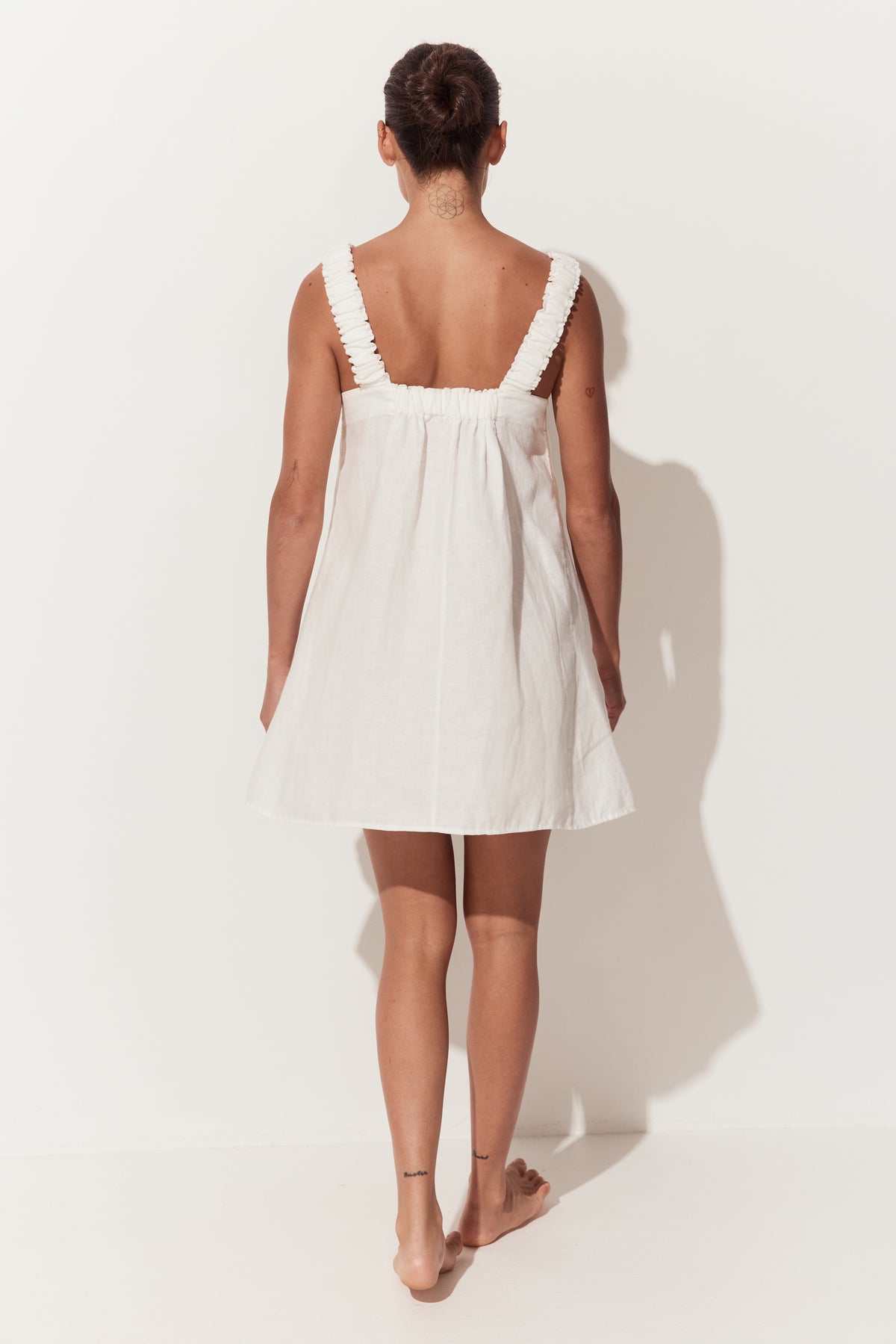 Zahra Linen Mini Dress in Ivory - back view while standing by a white studio wall - Lilly Pilly Collection