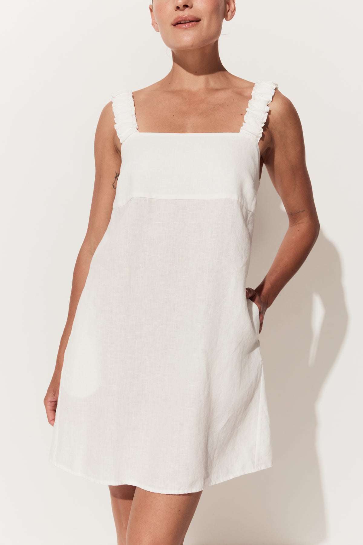 Zahra Linen Mini Dress in Ivory - close up view while standing by a white studio wall - Lilly Pilly Collection