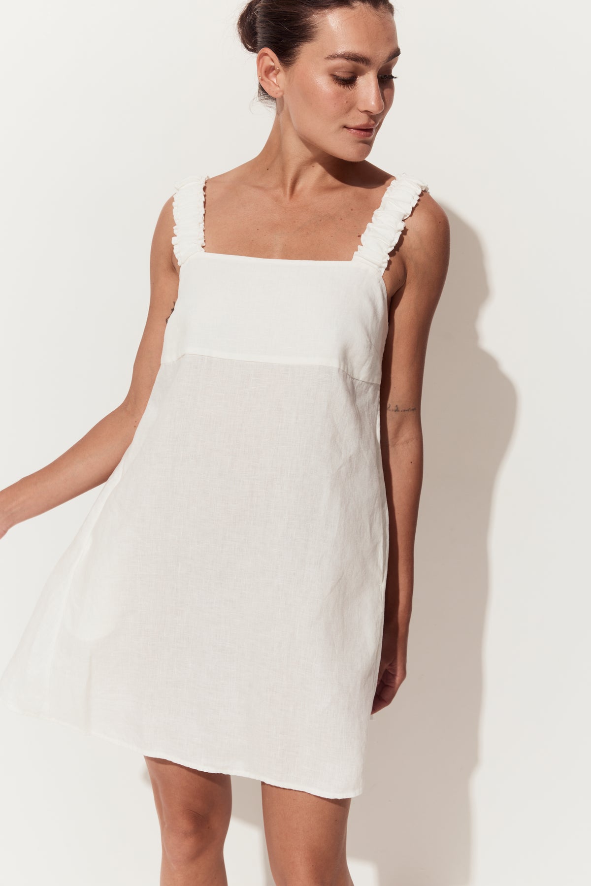 Zahra Linen Mini Dress in Ivory - three quarter view with arm to side in a white studio - Lilly Pilly Collection
