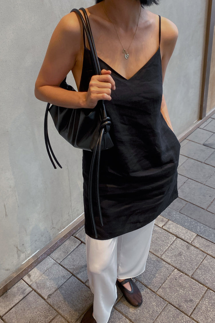 Liz Linen Mini Slip Dress in Black - close-up front view, V-neckline and thin straps, worn with tote bag, street setting - Lilly Pilly Collection