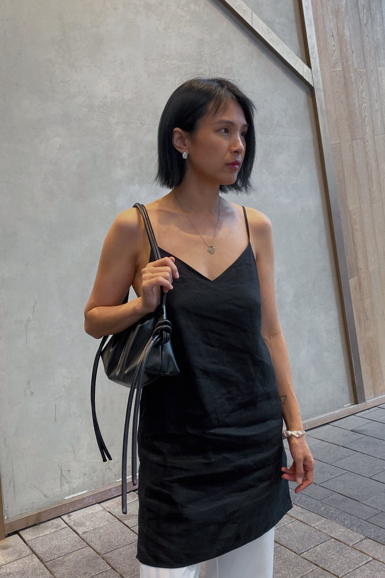 Liz Linen Mini Slip Dress in Black - front view, worn with tote bag over shoulder, layered over white trousers, street setting - Lilly Pilly Collection