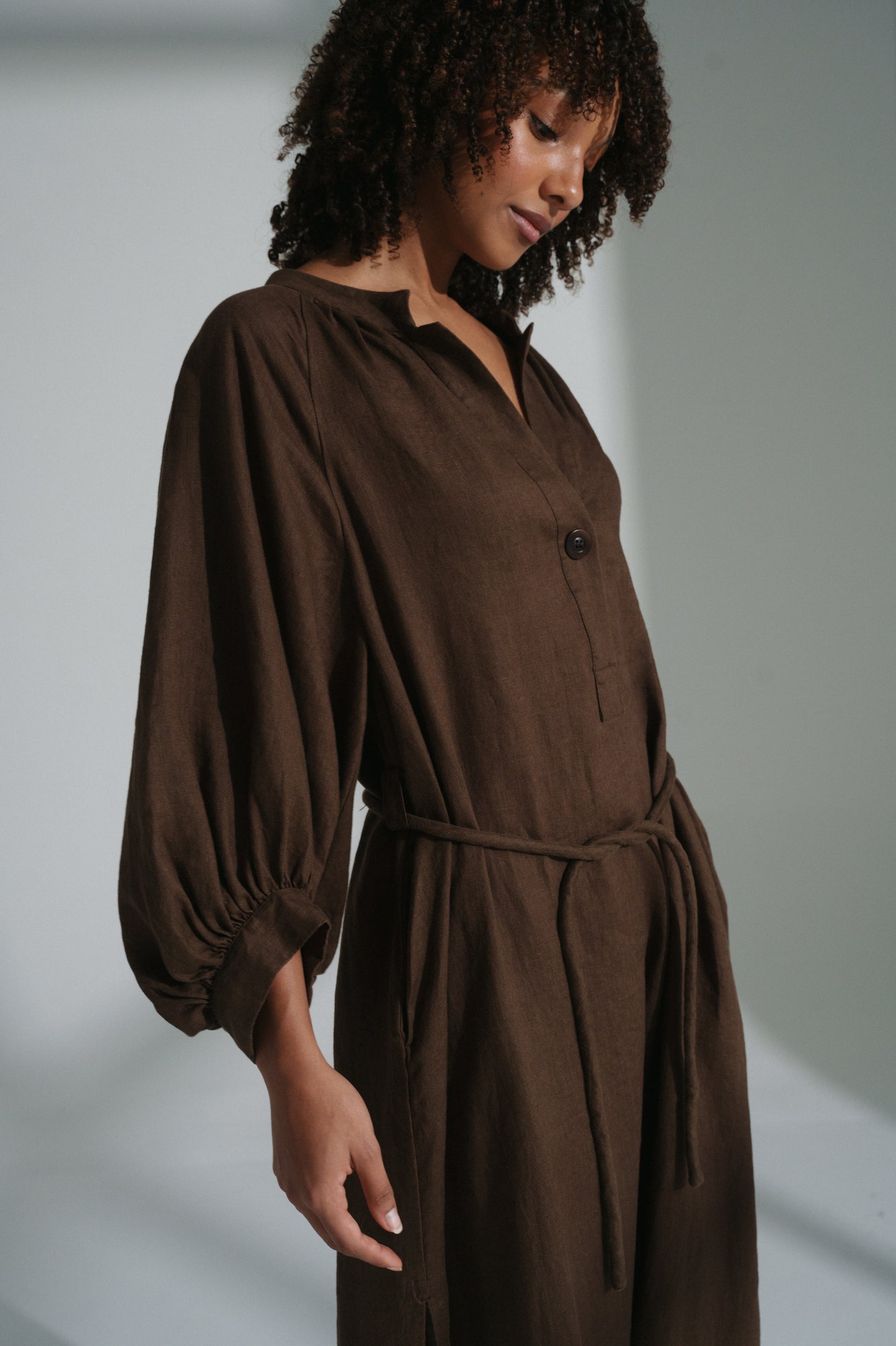 LILLY PILLY woman wearing a chocolate brown Mae linen dress standing in a softly lit room with a plain background