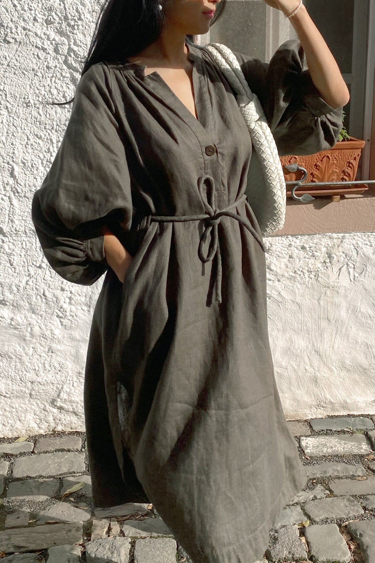 LILLY PILLY woman wearing a Mae khaki linen dress standing on a stone pavement.