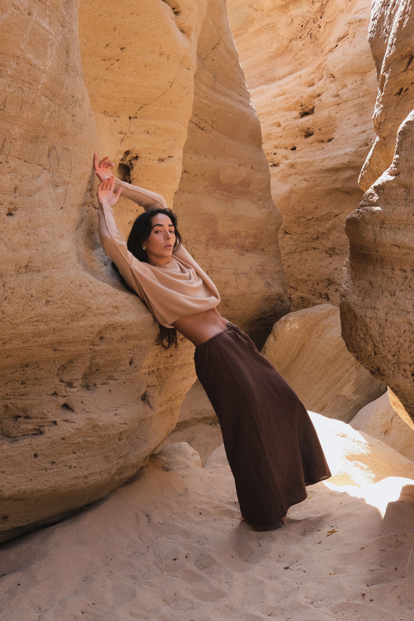 LILLY PILLY woman wearing Camel brown Miri cashmere knit sweater and chocolate brown Riley linen skirt posing against a rock wall in a desert canyon